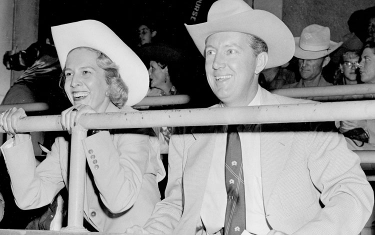 Jane and John Justin smile while cheering at a rodeo.